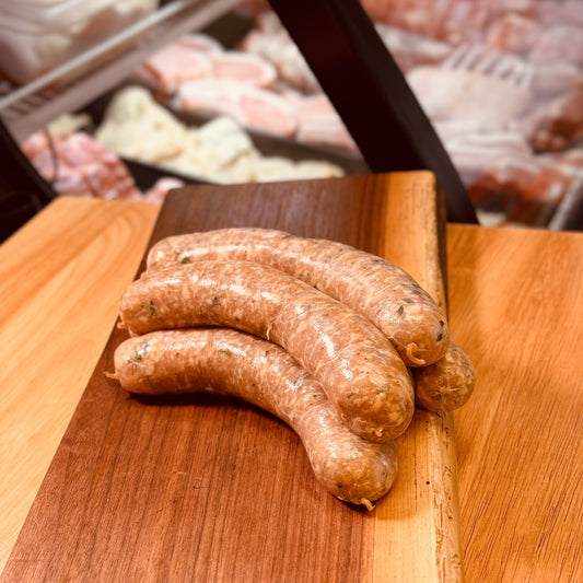 Three raw sausages on a wooden cutting board with a blurred background of a butcher shop.